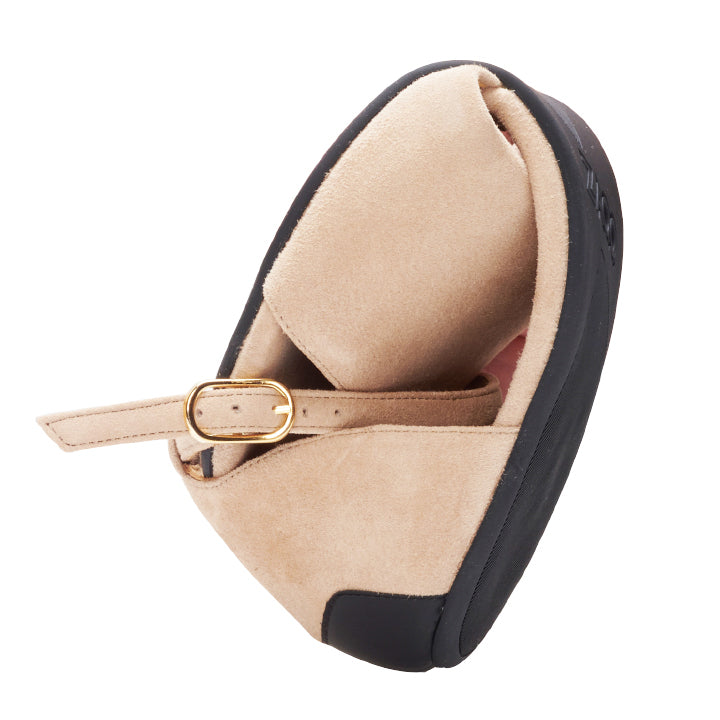 We present the TEQA Taupe from ZAQQ: A taupe loafer with a black sole and gold buckle strap, expertly crafted from suede. The angle shows the interior of the shoe and the intricate design details, further enhanced by the flexible sole for unrivaled comfort.