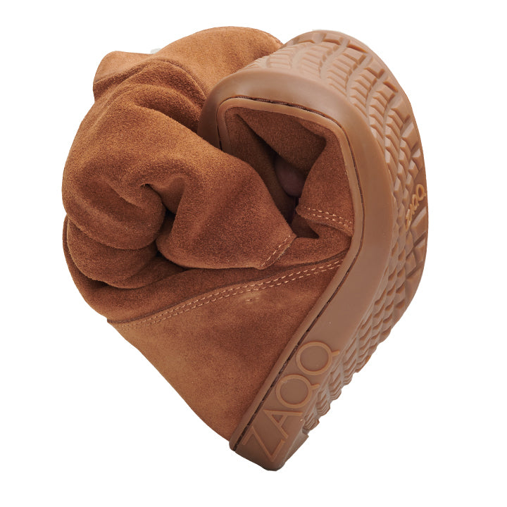 The TUQ Cognac shoe from ZAQQ can be bent in the middle and thus shows its flexibility. The sole, which features the TUQ logo, highlights the shoe's soft and pliable material, similar to the barefoot boot design.