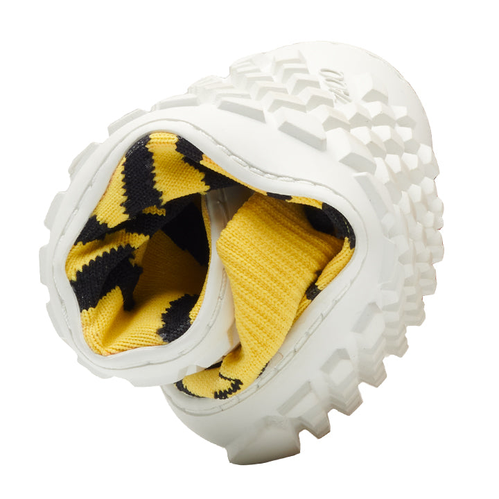 The white one ZAQQ SOQQ Tiger Yellow shoe is artfully twisted to highlight its flexible construction and features a textured sole. Its interior features a bold yellow and black pattern that creates a striking contrast to the exterior. This fashionable barefoot shoe presents itself gracefully against a pristine white background.