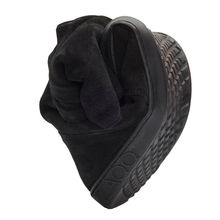 A pair of “TUQ Black” flip-flop sandals from ZAQQ made of black suede, crafted in an artistic and sculptural shape that highlights the textured sole pattern and strap details, emphasizing its unique flexibility and design.