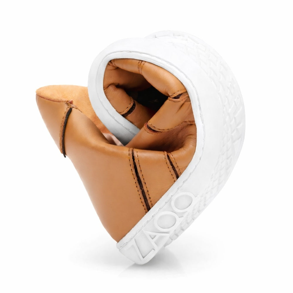 The QQQ Mid Sierra shoes from ZAQQ are elegantly twisted into a heart shape, which underlines their remarkable flexibility. These tan nappa leather shoes have white soles with textured patterns emblazoned with the brand's name ZAQQ is imprinted. Experience the exceptional barefoot shoe feel with every step in these expertly crafted shoes.