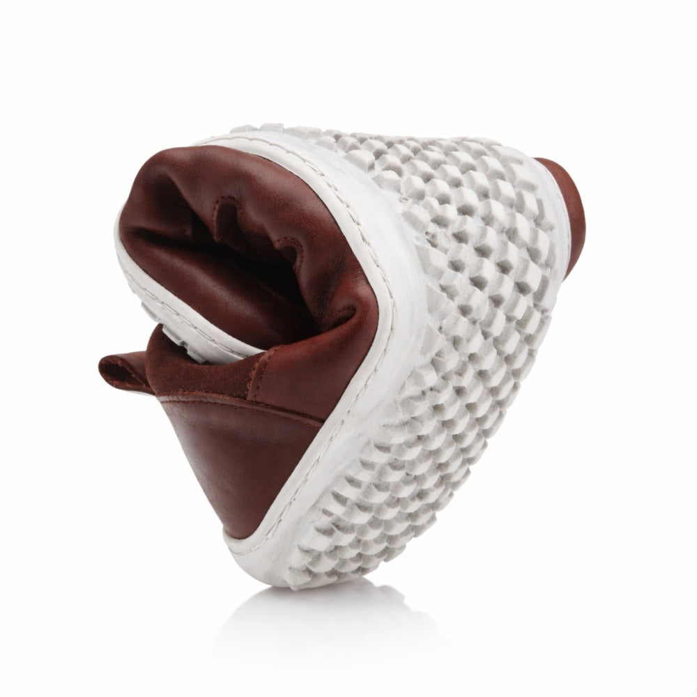 The SHOQQ Dark Brown from ZAQQ is a unique sneaker with a brown leather upper that has been expertly folded to reveal its impressive flexibility. Its sole features a striking black and white checkered pattern that underlines the shoe's distinctive design.