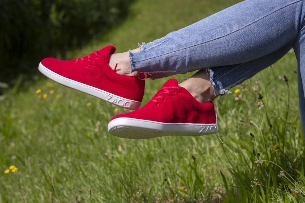 A person in LIQE Race Sneakers from ZAQQ and ripped blue jeans sits cross-legged over the lush grass. In the background you can see a green area with small yellow flowers, adding a fresh splash of color to the tranquil scene.