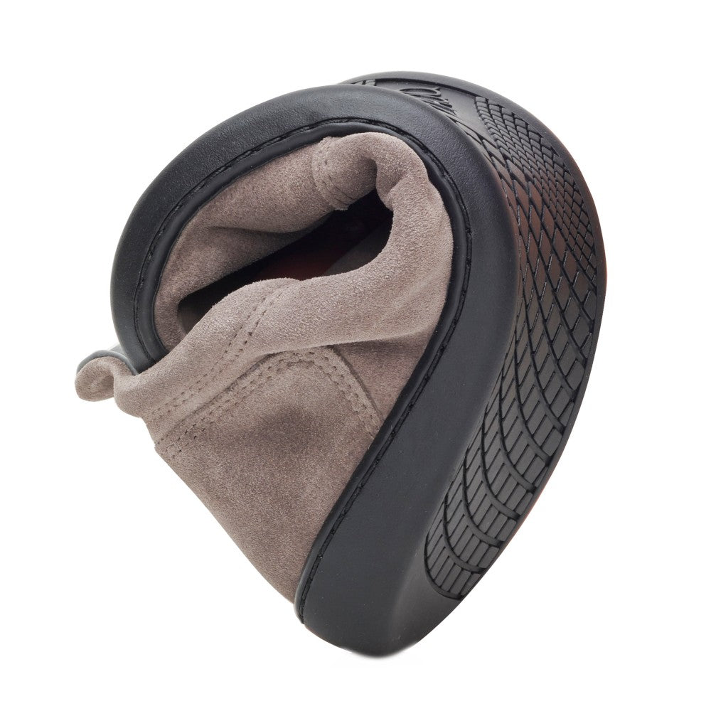 The PIQUANT Velor Gray from ZAQQ Showcasing its flexibility by bending in the middle, it features a soft tan suede upper and a black rubber sole with a textured grip pattern for superior comfort.