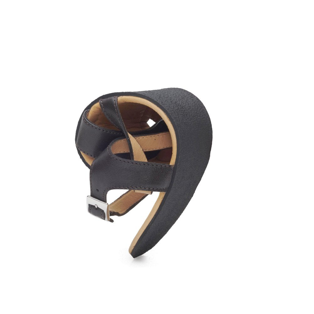 The QEE Dark Brown sandal from ZAQQ is a chic leather creation with a distinctive twist, featuring exposed straps and a buckle elegantly presented against a white background. This fashionable barefoot sandal features a rubber sole that ensures ultimate comfort and flexibility.