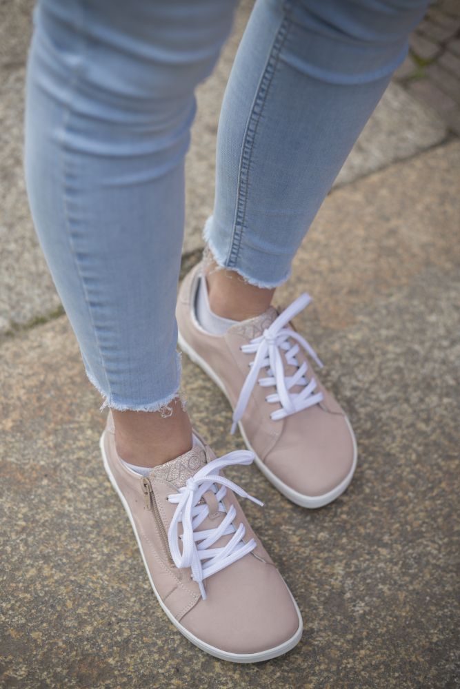 A person in light blue jeans and stylish ZAQQ QOMFY Wide Pink Sneakers with white laces confidently strolls across the stone pavement.