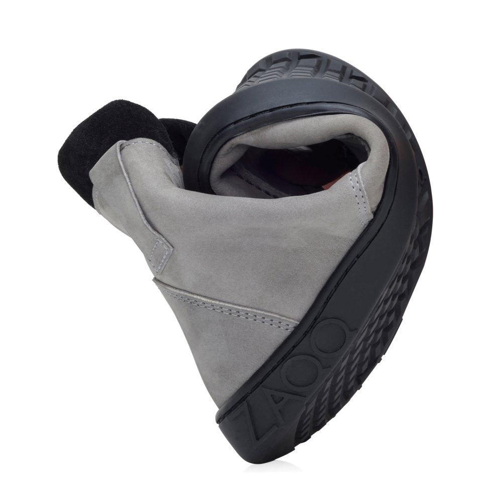 The ROQA Gray shoe is curved to demonstrate its flexibility and offers flexible comfort. It features a dark sole and a light gray upper. The brand name ZAQQ is embossed into the sole and underlines the design and comfort of the shoe, which is reminiscent of barefoot shoes.