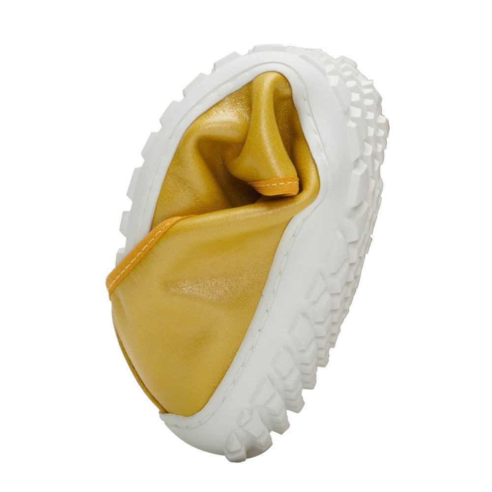 The SUQAR Kiwi from ZAQQ with its yellow design and white, robust sole is rolled up into a ball and thus shows its flexibility. The texture and material of the shoe are visible, highlighting its soft and pliable nature.