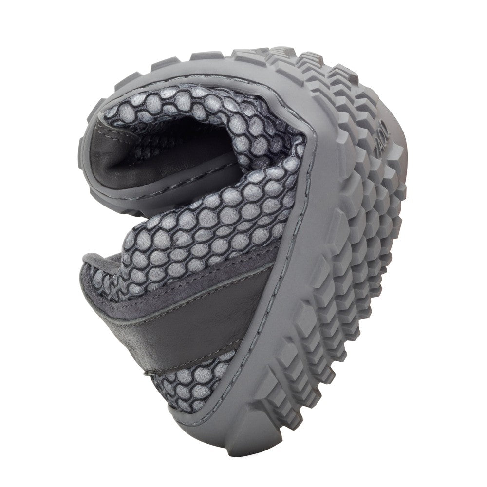 The TOQIO Gray from ZAQQ Shows off its flexibility by folding in half, showcasing the textured grip of its sole and breathable mesh upper. The design emphasizes comfort and durability.