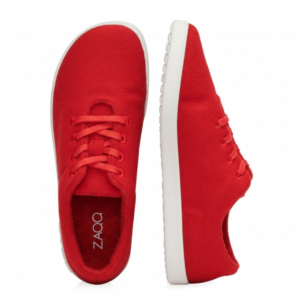 A pair of red casual LIQE race sneakers from ZAQQ with rubber sole. One shoe is seen from above and shows the laces, while the other is seen from the side and the sole with the inscription ZAQQ highlights. The simple white background emphasizes the elegant design and the comfortable barefoot sole.