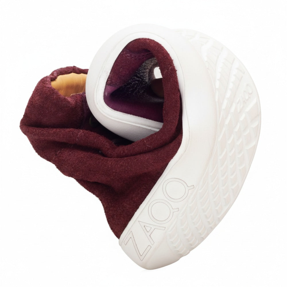 A flexible, maroon sneaker is twisted into a compact spiral, revealing its sole with the ZAQQ-Logo. Showcasing its flexibility and unique construction, the QORE High Mazarine design skillfully combines suede and smooth leather for added style.