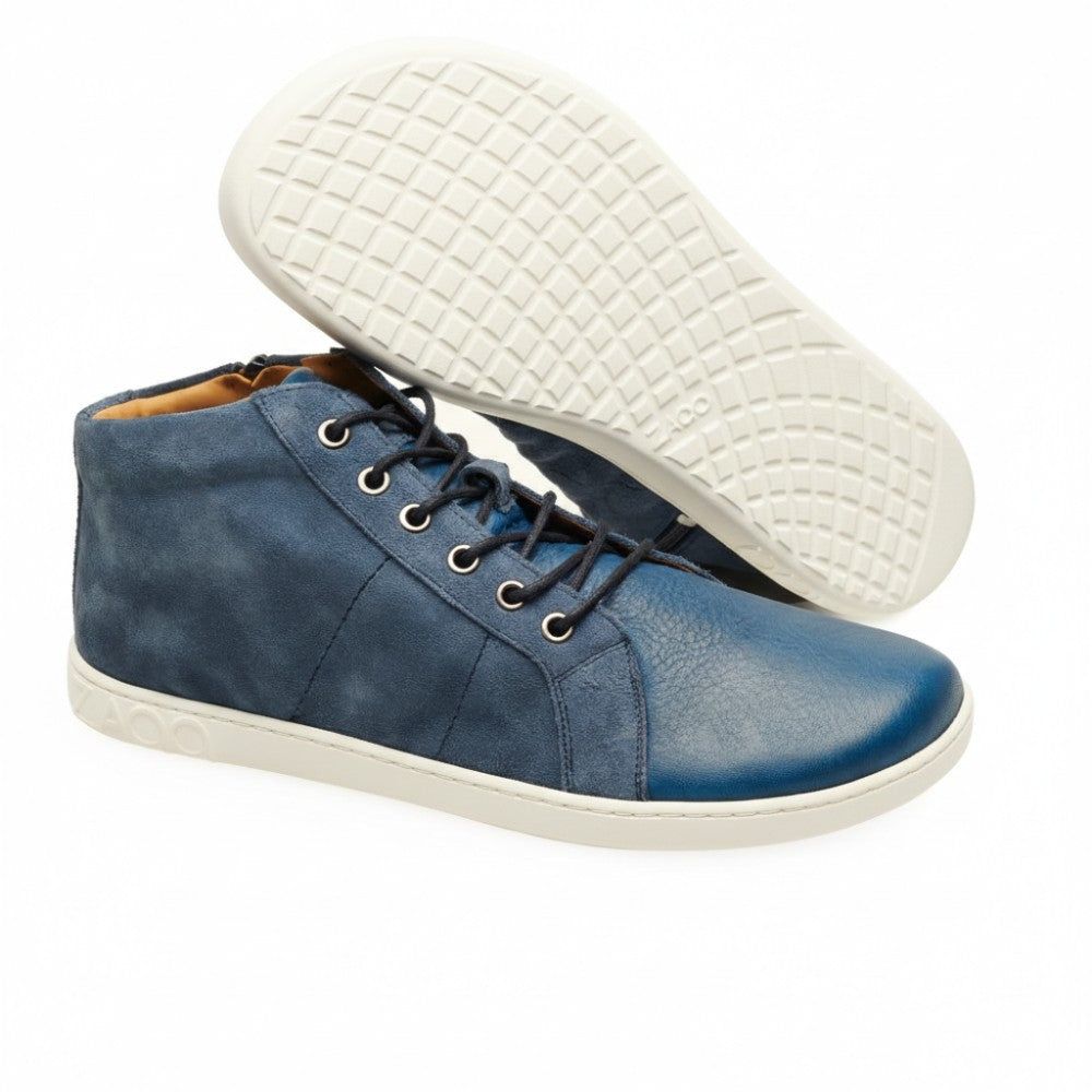 Der QORE Mid Deep Sea von ZAQQ präsentiert ein Paar blaue High-Top-Sneaker mit weißer Sohle aus Veloursleder. Ein Schuh wird aufrecht präsentiert, während der andere auf der Seite liegt, wodurch das detaillierte strukturierte Sohlendesign dieser blauen Sneaker hervorgehoben wird.
