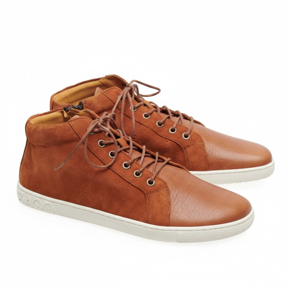 We present the sophisticated QORE Mid Sierra from ZAQQ, Made from different types of leather for an elegant appearance. These brown leather high-top sneakers feature white soles and tan interiors, complemented by casually knotted laces. The brand name is expertly embossed near the heel for additional distinguishing features.