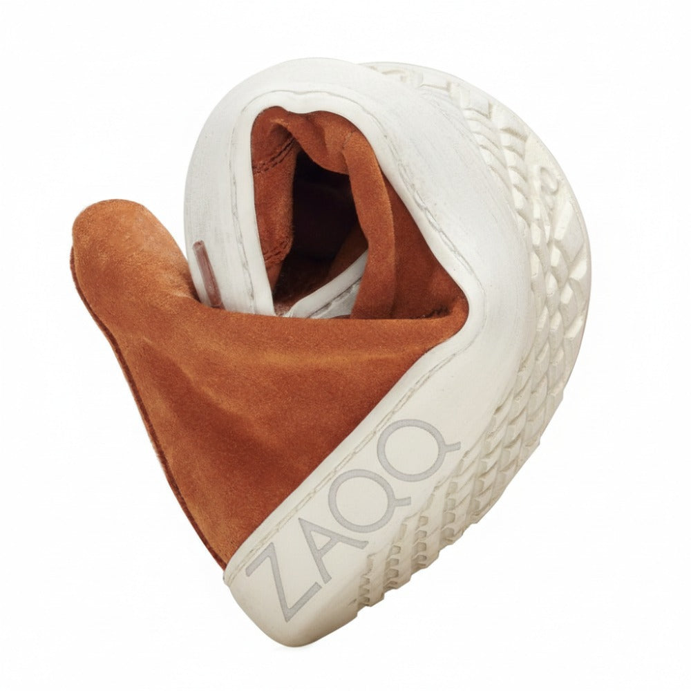 The QORE Mid Sierra sneaker from ZAQQ is elegantly folded in half and presents its white exterior with textured sole and brown interior.