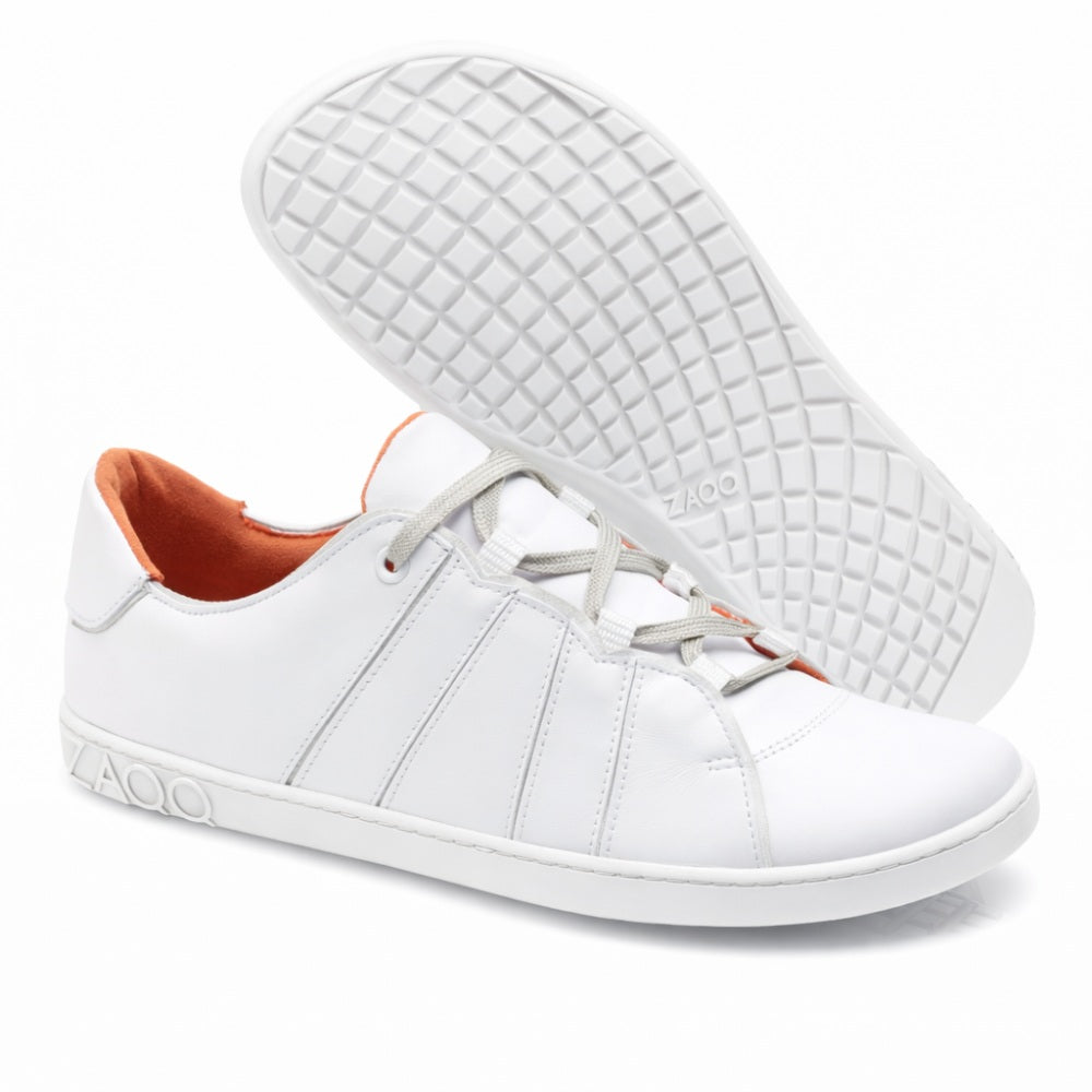 Introducing the QQQ Low White Sneakers from ZAQQ, an elegant pair made of high-quality nappa leather. These casual shoes have gray laces and a bright orange interior. The design includes intricate side seams, with one shoe standing upright and the other tilted to reveal the waffle pattern sole. The brand name ZAQQ can be clearly seen on both the side and the sole and underlines the characteristic barefoot shoe design.