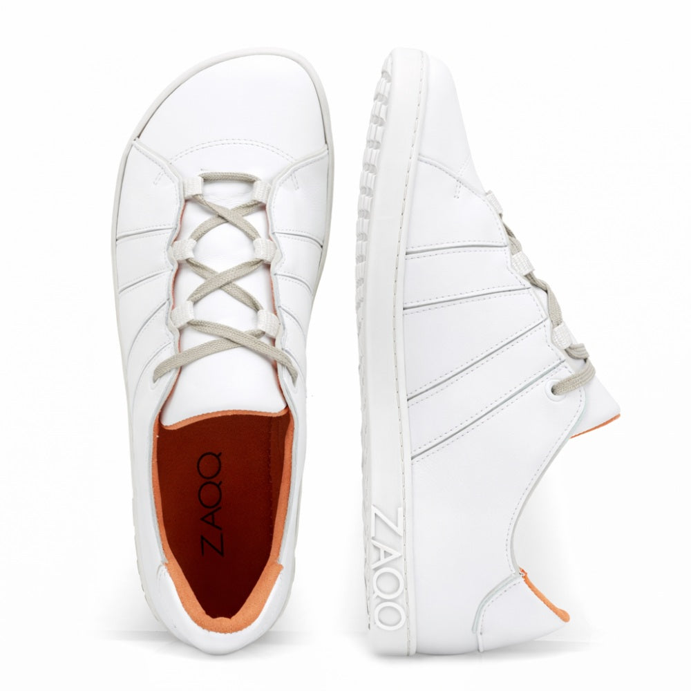 Introducing the QQQ Low White: a pair of white sneakers with gray laces and bright red lining, expertly crafted from breathable premium nappa leather. These shoes are clearly marked on the side and sole ZAQQ-Branding provided. Against a white background, one shoe is seen from above while the other is shown in side profile, highlighting the barefoot shoe design.