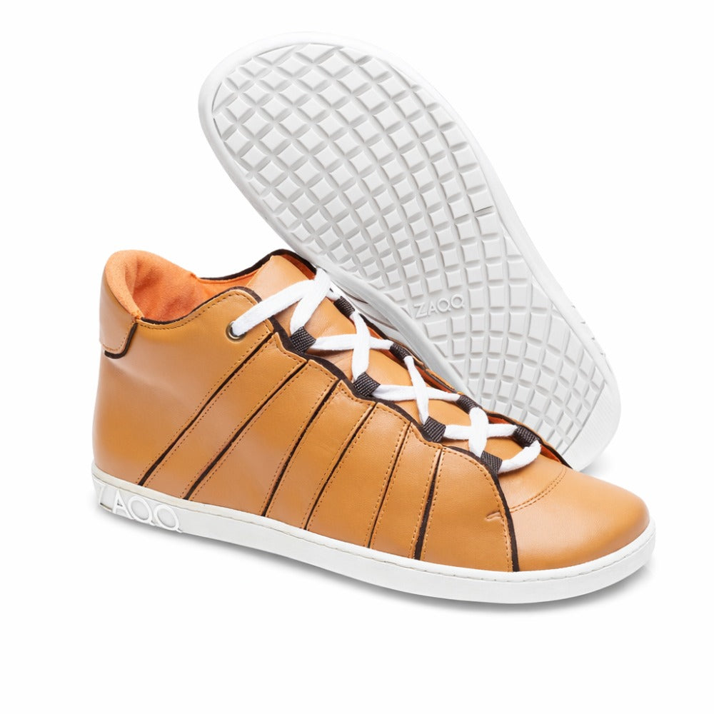 The QQQ Mid Sierra from ZAQQ is a pair of high-top sneakers in brown, made from high-quality nappa leather. They feature white laces and soles; one shoe stands upright while the other leans against it, highlighting the tread pattern. The brand name ZAQQ adorns both the side and the sole and provides a comfortable barefoot-like feel.