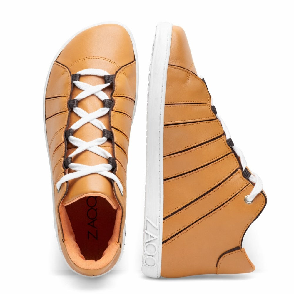 Introducing the QQQ Mid Sierra from ZAQQ: a stylish pair of high-top sneakers in tan, expertly crafted from luxurious nappa leather. Featuring white soles and laces with striking black accents, these shoes proudly display the brand name ZAQQ on the page. One shoe features a top view of its laces, while the other features its striped design inspired by barefoot shoes.