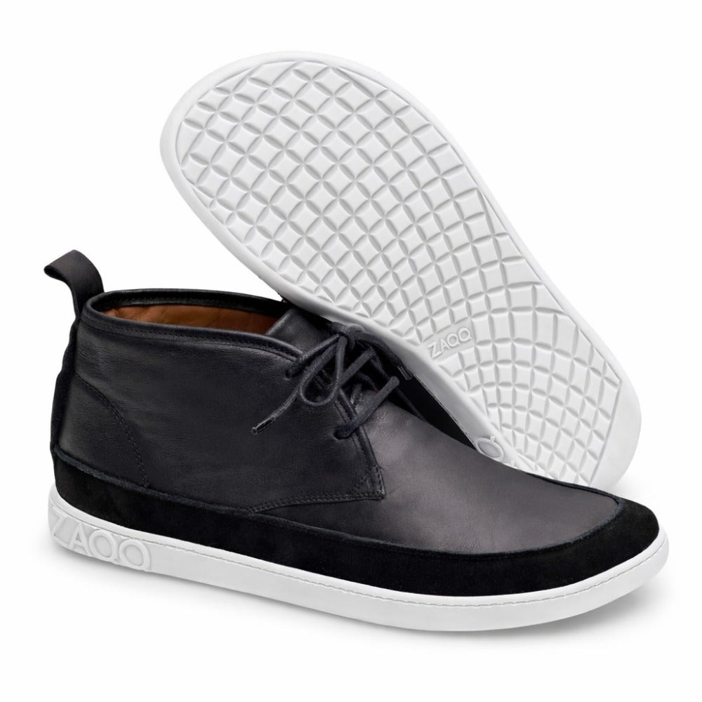 A pair of stylish black ones ZAQQ QUITMAN high-top sneakers with contrasting white soles. One sneaker stands upright and shows off both the side and front profile, while the other lies down and has a textured sole with the ZAQQ-Branding highlights.