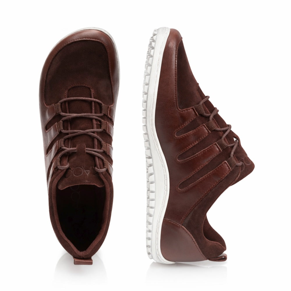 By the shoes ZAQQ SHOQQ Dark Brown one shoe stands upright and the other lies on its side, highlighting the textured sole. Crafted from a mix of leather and suede, these brown casual shoes feature a lace-up front, making them an excellent choice for sneaker fans who appreciate both style and comfort.