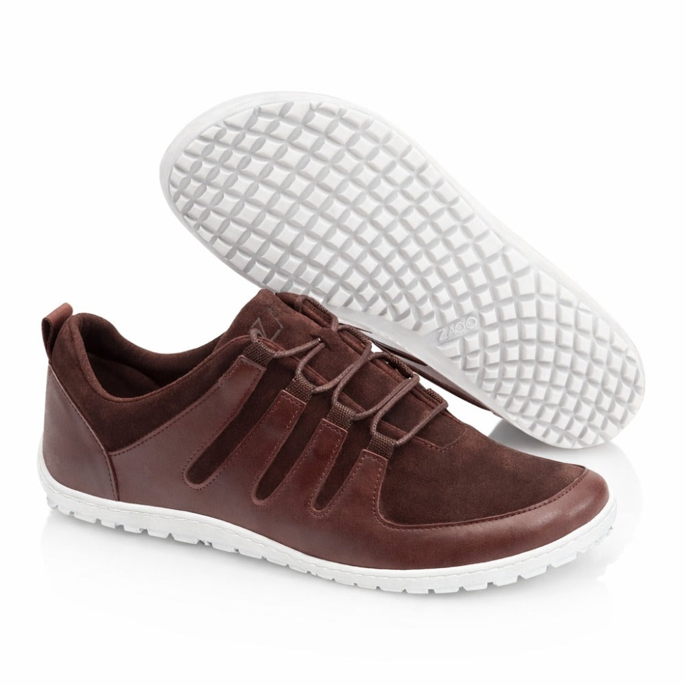 The ZAQQ SHOQQ Dark Brown sneakers combine leather and suede for a chic look, finished off with white rubber soles. These barefoot shoes feature decorative laces and a simple slip-on design, with one shoe highlighting the grid pattern on its sole.