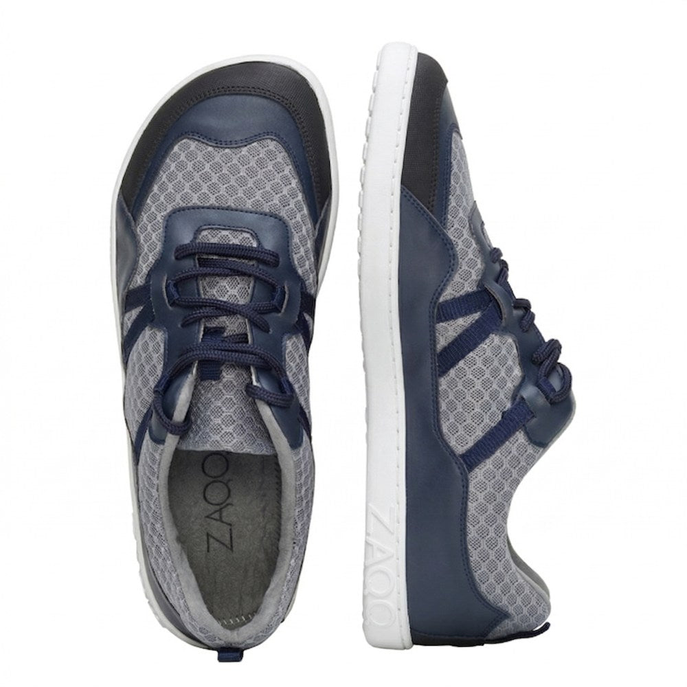 We present the ZAQQ SQATE Gray trainers – a pair of gray and navy trainers ideal for any active day. These women's sneakers feature a breathable mesh pattern, white soles and dark blue laces. One shoe stands upright, the other shows off its slim side profile, combining style with comfort.