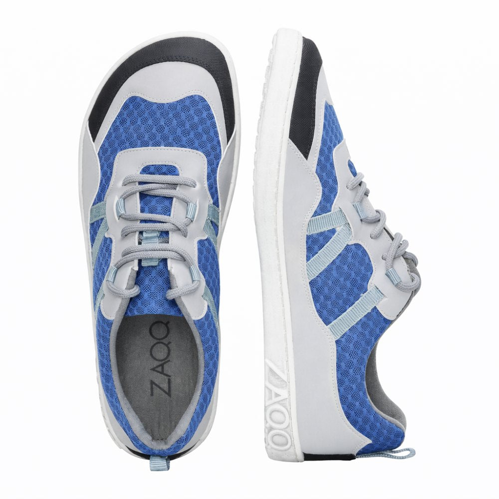 Wir präsentieren den SQOTT Blue von ZAQQ – ein stilvolles Paar sportlicher Sneaker in einem auffälligen Farbschema aus Blau und Grau mit weißen Sohlen. Ein Schuh steht aufrecht, um sein Seitenprofil schön zur Geltung zu bringen, während der andere so positioniert ist, dass er eine Draufsicht bietet. Das Design umfasst ein einzigartiges sechseckiges Muster mit grauen Schnürsenkeln, das Stil und atmungsaktiven Komfort nahtlos miteinander verbindet, perfekt für Ihren aktiven Lebensstil.