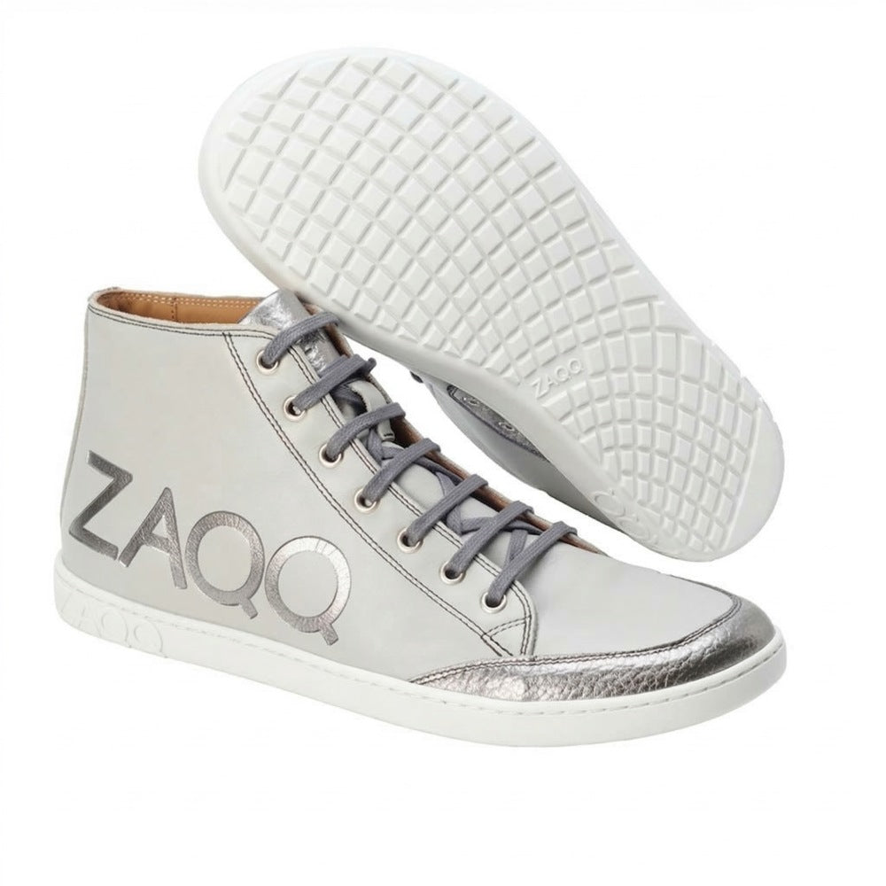 We present the SQYLA Gray from ZAQQ, a pair of high-top nappa leather sneakers. These stylish shoes have gray laces, a striking silver toe cap and the eye-catching ZAQQ-Brand logo on the side. Designed with a rubber sole for excellent grip, they feature a white base complemented by metallic accents for a sleek and modern appearance.