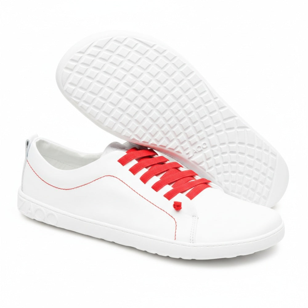 Ein Paar weiße STIQ-Sneaker von ZAQQ mit roten Schnürsenkeln und grau strukturierter Sohle. Ein Schuh steht aufrecht, während der andere angehoben ist, um das Sohlenmuster zu zeigen. Die Marke ZAQQ ist deutlich auf der Seite der Sohle zu sehen.