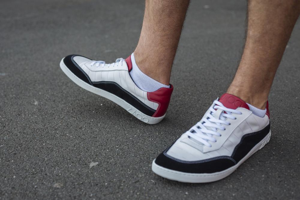 Nahaufnahme einer Person, die die ZAQQ QAMPION Black White Sneakers trägt und auf einer grauen Asphaltoberfläche steht.